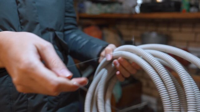Professional electrician's hands pulling a steel wire through a flexible corrugated pipe to prepare for installing electrical cables during a construction or renovation project