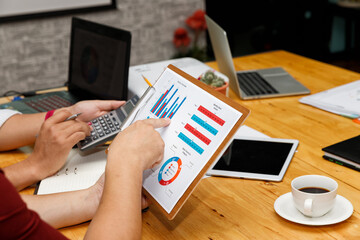 Group of people working on financial audit with laptop and tablet. Strategic planning meeting with coffee cup on wooden table.
