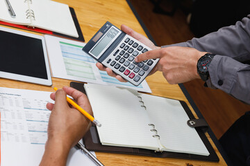 Professional accountant calculating tax and reviewing financial documents with client. Business meeting concept with tablet, paperwork, and investment strategy planning.