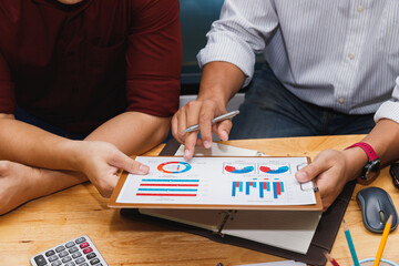 Two business men discussing financial data on clipboard. Team analyzing market share pie chart with pen during meeting.