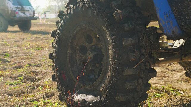Close-up on a UTV wheel covered in mud. Vehicle is on rough dirt terrain, suggesting an off-road race or competition. Gritty, action-oriented scene with natural light