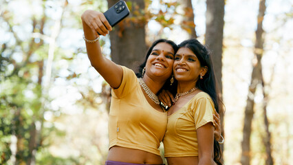 Two smiling indian women friends taking a selfie with a smartphone, wearing traditional clothing...