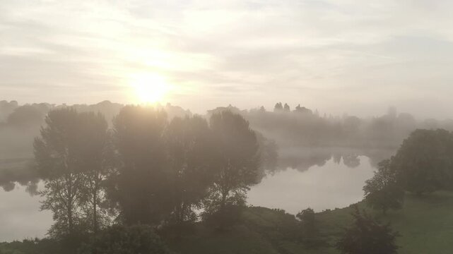 Aerial view of fog-laden trees and water bodies under the diffused sunlight, a serene landscape, Ripley, England, United Kingdom.