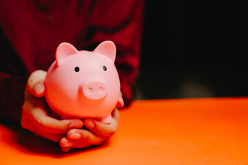 Saving concept. Pink piggy bank hands saving money finance investment protection orange table dark...