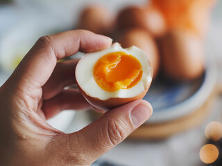 Soft boiled egg in hand with runny yolk and blurred background plate of eggs