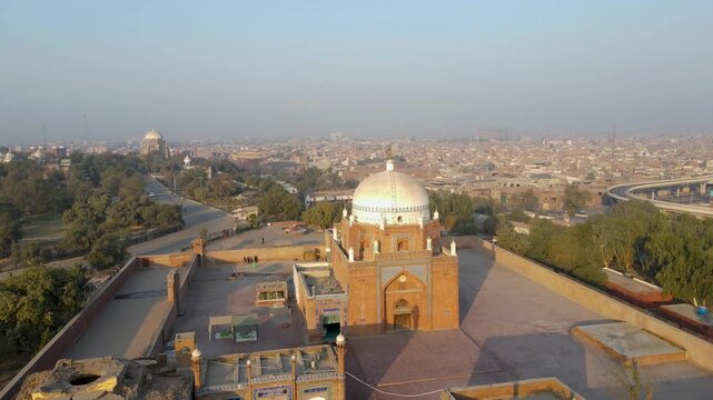 Aerial view of the Shrine of Bahauddin Zakariya, with its red brick structure and white dome, contrasting with the city's muted tones, Multan, Punjab, Pakistan.