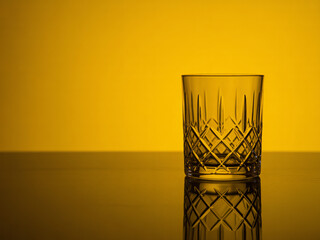 Luxury crystal whiskey glass on reflective surface with golden light