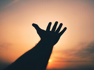 Silhouetted hand reaching towards vibrant sunset sky
