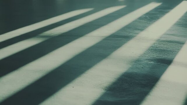 Sunlight beams streaming through a window onto a textured floor surface, forming a striking pattern of bright light stripes and dark shadows, providing an abstract background