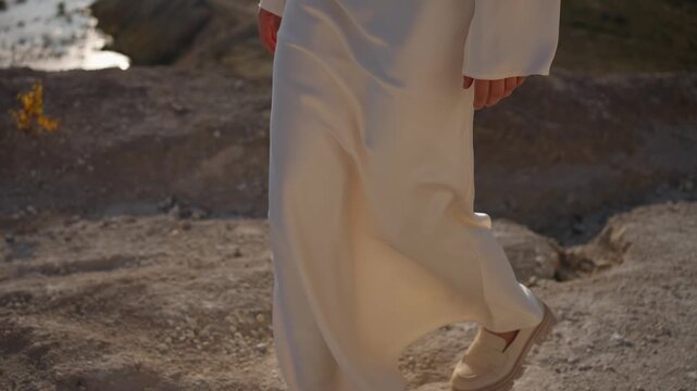A woman in a white dress walks along the riverbank. The concept of a female gait.