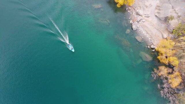 Aerial view of a lone boat cutting through the turquoise waters near the rocky shore and golden trees of Upper Kachura lake, Skardu, Gilgit, Pakistan.