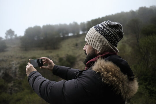 A bearded man contemplates the landscape of trees and mist on a foggy winter day.