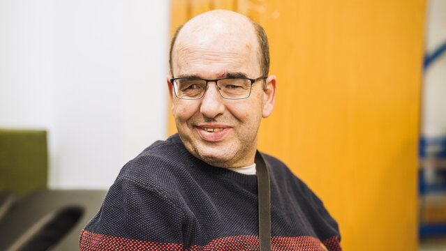 Man with glasses and a disability smiling warmly, representing concepts of inclusion, diversity, community, and support for people