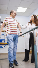 Obraz premium Man in therapy session with female physical therapist at rehabilitation center. Patient using parallel bars for recovery support