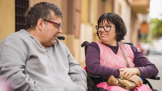 Two diverse people using wheelchairs engaged in cheerful conversation, promoting concepts of friendship, disability inclusion, and accessibility