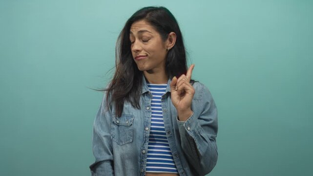 Woman wearing denim shirt and striped top pointing index finger toward camera in teal studio; skepticism warning.