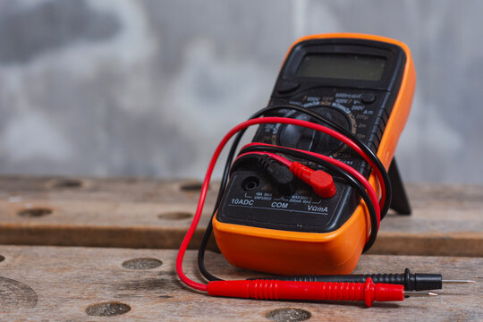 Digital multimeter with red and black test leads placed on wooden workbench. Concept of electrical testing, electronics repair, measurement equipment, electrician tools and engineering work.