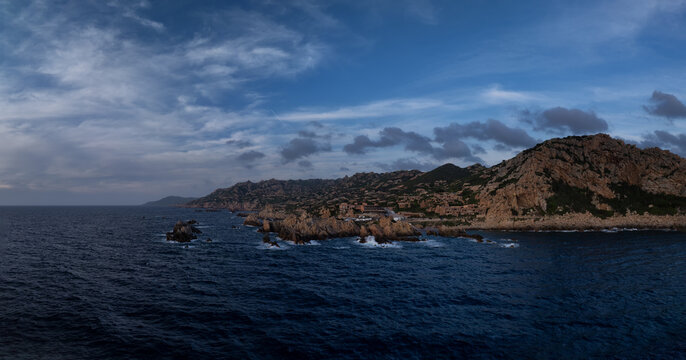 Aerial view of rugged cliffs meet the sapphire sea, waves crashing against the rocky shore, a dramatic landscape under a moody sky, Costa Paradiso, Sardegna, Italy.