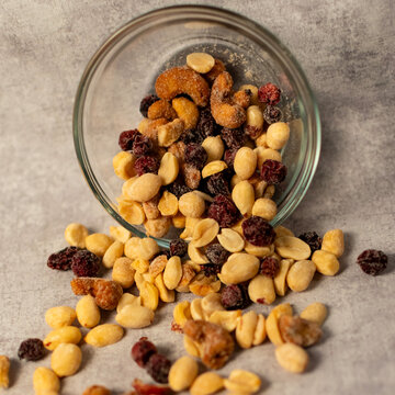 Front view of trail mix falling from a small glass bowl. 