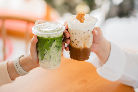 Hands of  female and male holding glass of ice coffee and ice matcha green tea together at cafe.