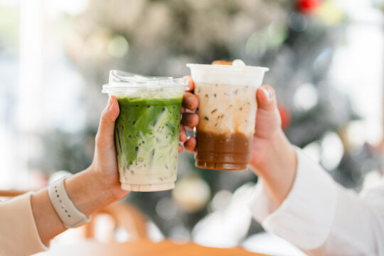 Hands of  female and male holding glass of ice coffee and ice matcha green tea together at cafe.