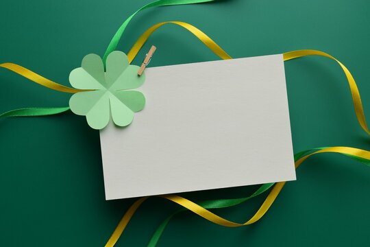Blank greeting card with green paper clover and satin ribbon on green background