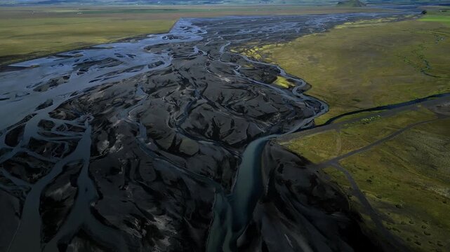 Aerial view of a river delta displaying contrasting colors and textures, where dark sediments meet the green landscape, Svinafell, Sveitarfelagio Hornafjorour, Iceland.