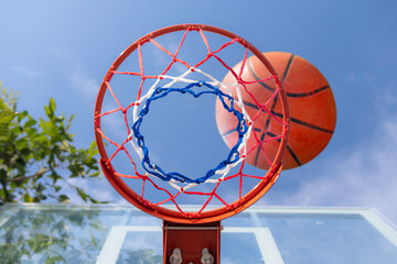 Shooting basketball into basketball hoop with a net stands against a clear blue sky on a sunny day at an outdoor playground court, ready for a recreational game of sport © noppadon