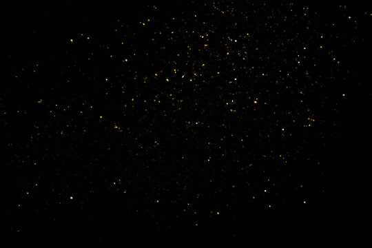Golden flakes-glittering gold particles are scattered on the black surface. material for art design.