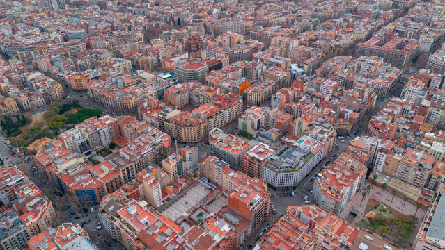 Aerial view of a dense urban tapestry where buildings with terracotta rooftops interlock in a geometrical harmony, creating an intricate mosaic of urban life, Barcelona, Catalonia, Spain.
