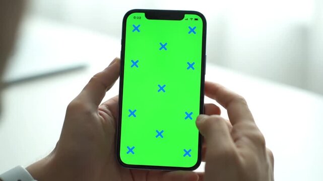 Hands holding smartphone with green screen and blue crosses for chroma key