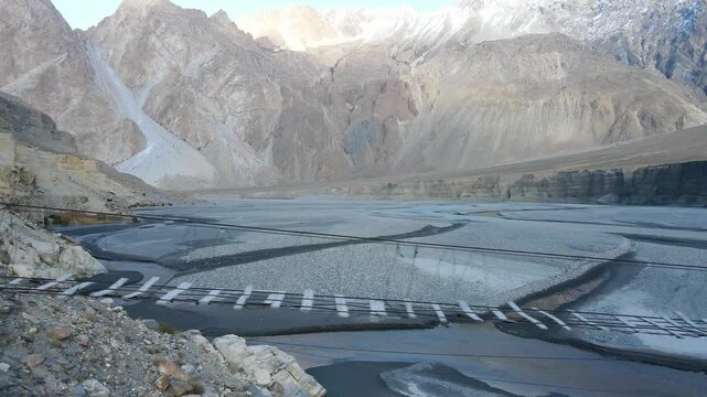 Aerial view of the Hussaini Suspension Bridge over the river with a backdrop of stark mountains, creating a striking contrast, Hunza, Gilgit, Pakistan.