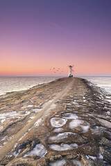 lighthouse on a stone pier in sunset light in winter season