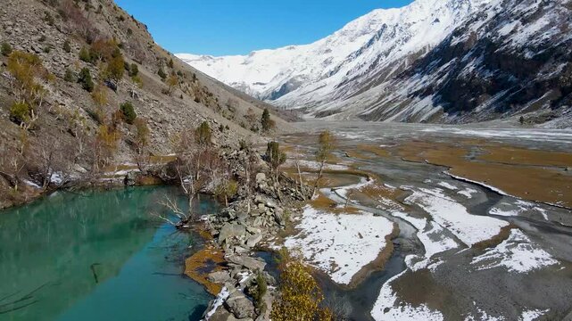 Aerial view of the turquoise Naltar lake surrounded by rocky mountains and snow-capped peaks creating a stunning contrast of colors, Hunza, Gilgit, Pakistan.