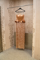 A designer-designed evening gown made of orange sequins and satin, hanging on a hanger. (stock photo)