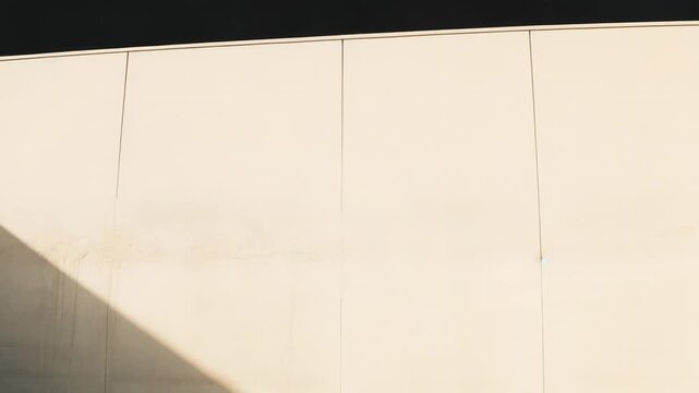 Modern concrete wall surface showing a strong diagonal composition with contrasting areas of bright sunlight and deep shadow, creating a dynamic background texture