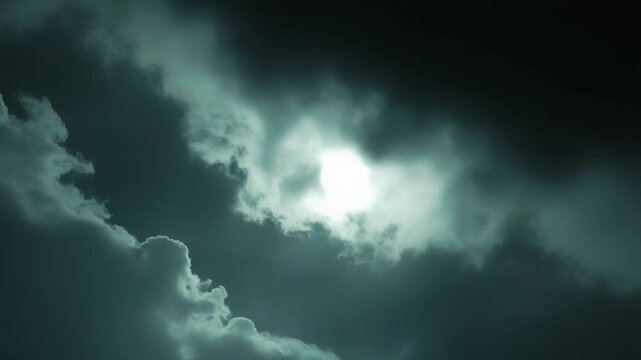 Full moon glowing brightly behind dark, dramatic clouds, creating a mysterious and atmospheric night sky scene with a dramatic play of light and shadow