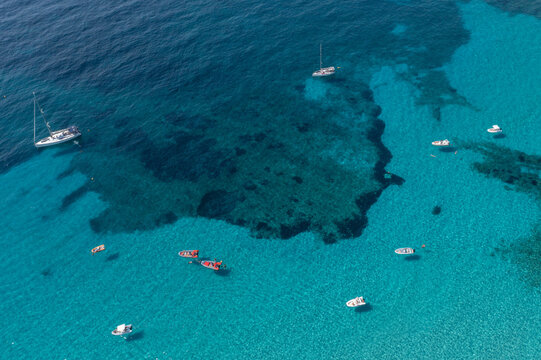 Aerial view of turquoise waters embrace boats, revealing dark patches beneath the surface, like secrets in the deep, Sardinia, Italy.
