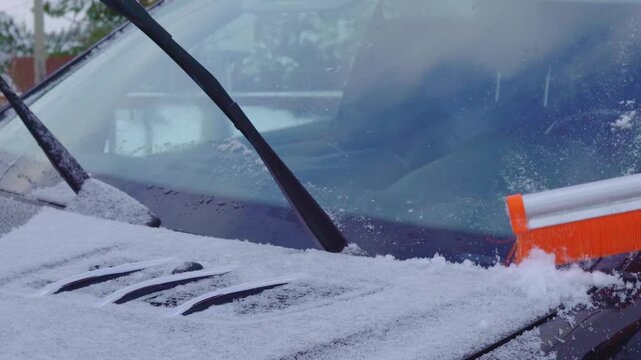 Clearing snow from car windshield. Winter morning preparation.