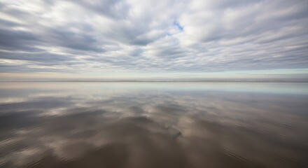 Vast tranquil ocean beach with reflections of cloudy sky on wet sand at low tide