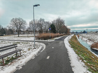 Asphalt Bicycle trail in the winter in the town. Brook with a frozen shores. Led lamp
