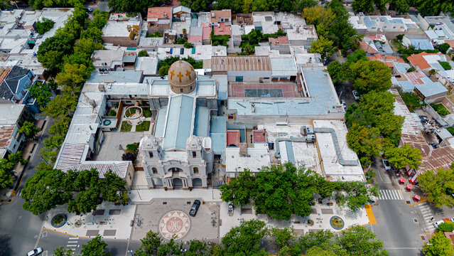 Aerial view of a grand cathedral with its ornate dome and towers, framed by lush green trees and geometric buildings, Lujan de Cuyo, Mendoza, Argentina.