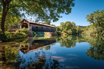 Obraz premium Historic covered bridge gracefully spans a calm river in a serene natural setting during daytime