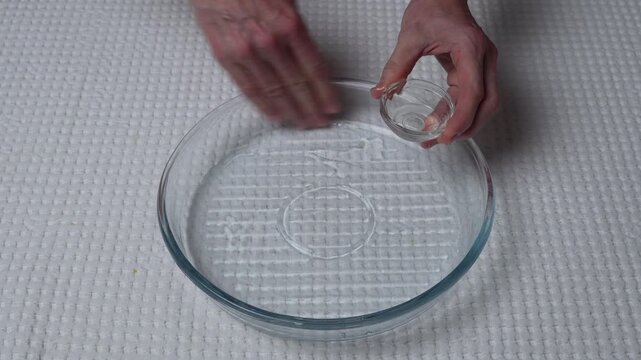 Oiling glass baking dish before baking. Hands greasing a round glass baking dish with vegetable oil. Close-up baking preparation on a white tablecloth.