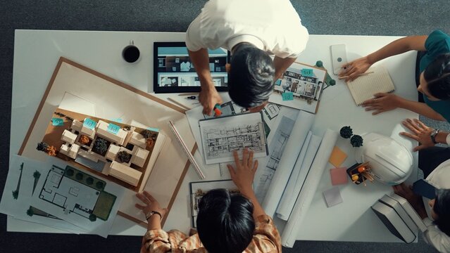Top view of project manager working together to brainstorm house design while standing around meeting table with project plan and blueprint. Aerial view of designer team explain project. Alimentation.