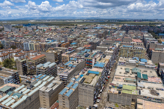 Aerial view of dense urban sprawl punctuated by varied building heights and textures under a vast sky, vibrant yet gritty with Jomo Kenyatta International Airport in the background, Nairobi, Kenya.