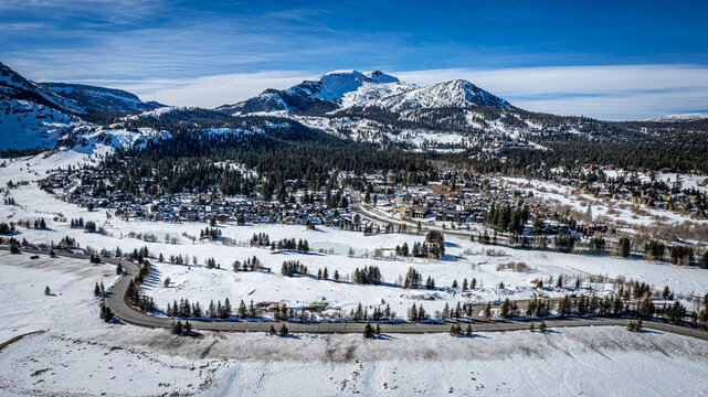 Aerial view of snow-dusted landscapes meet the quaint town nestled beneath the majestic, snow-capped mountains under a crisp, clear sky, Mammoth Lakes, California, United States.