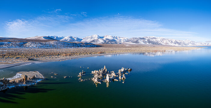 Aerial view of tufa towers rising starkly from the tranquil, emerald waters of Mono Lake against a backdrop of snow-capped mountains, Lee Vining, California, United States.