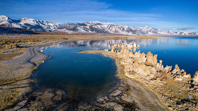 Aerial view of the tufa towers rising from the serene, reflective waters of Mono Lake, contrasted against the snow-capped Sierra Nevada mountains, Lee Vining, California, United States.