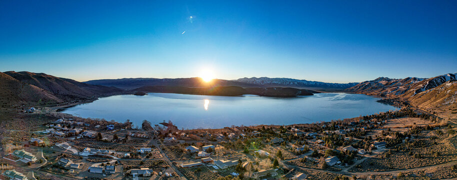 Aerial view of the sun rising over the still, reflective waters of Topaz Lake, nestled among the rugged Nevada landscape, Topaz Lake, Nevada, United States.